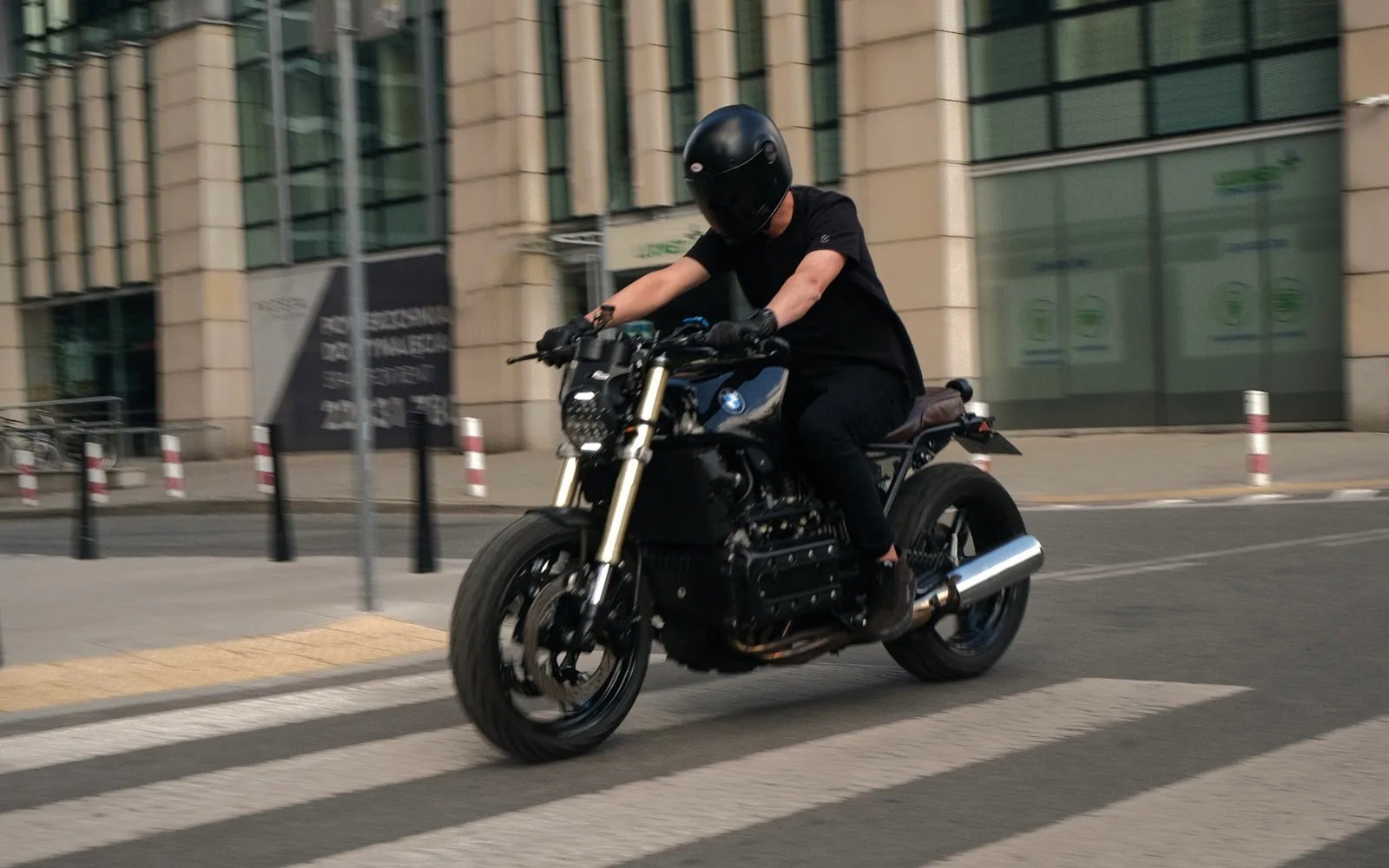 Ludovic riding his black BMW K1100 brat across a zebra crossing in central Warsaw