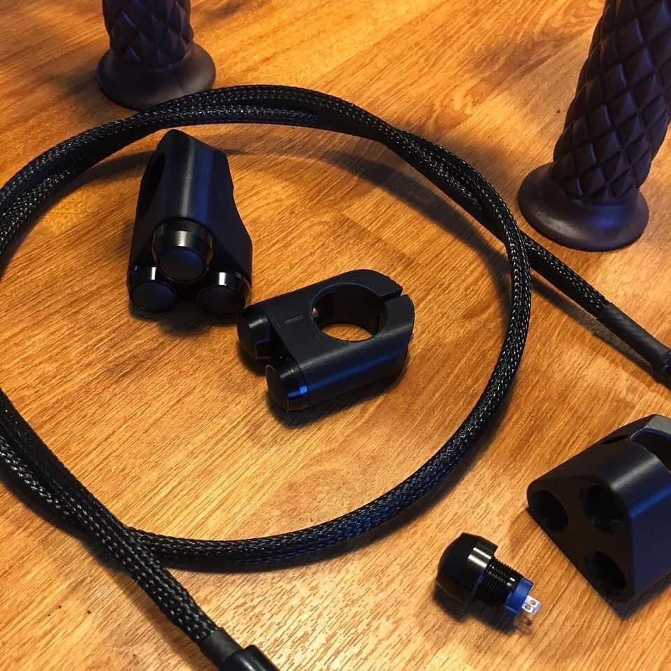 3D printed handlebar button housings with microswitches, braided wiring loom and grips laid out on a workbench