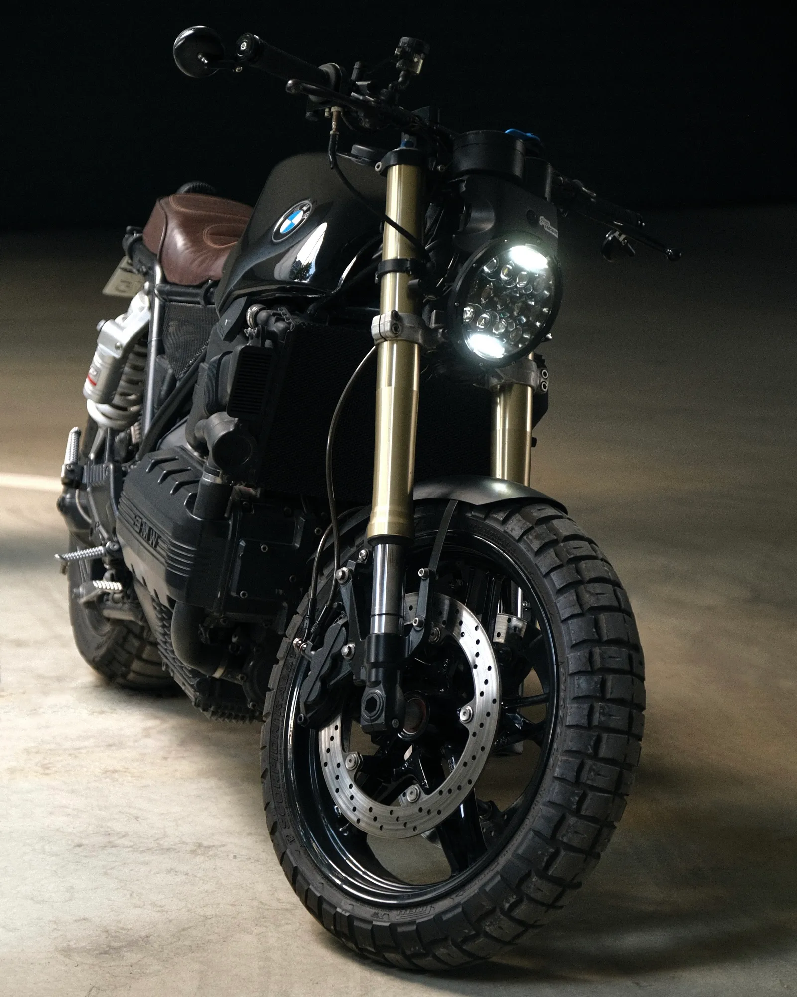 Studio-lit front view of the black K1100 with LED headlight on, gold forks and brown seat