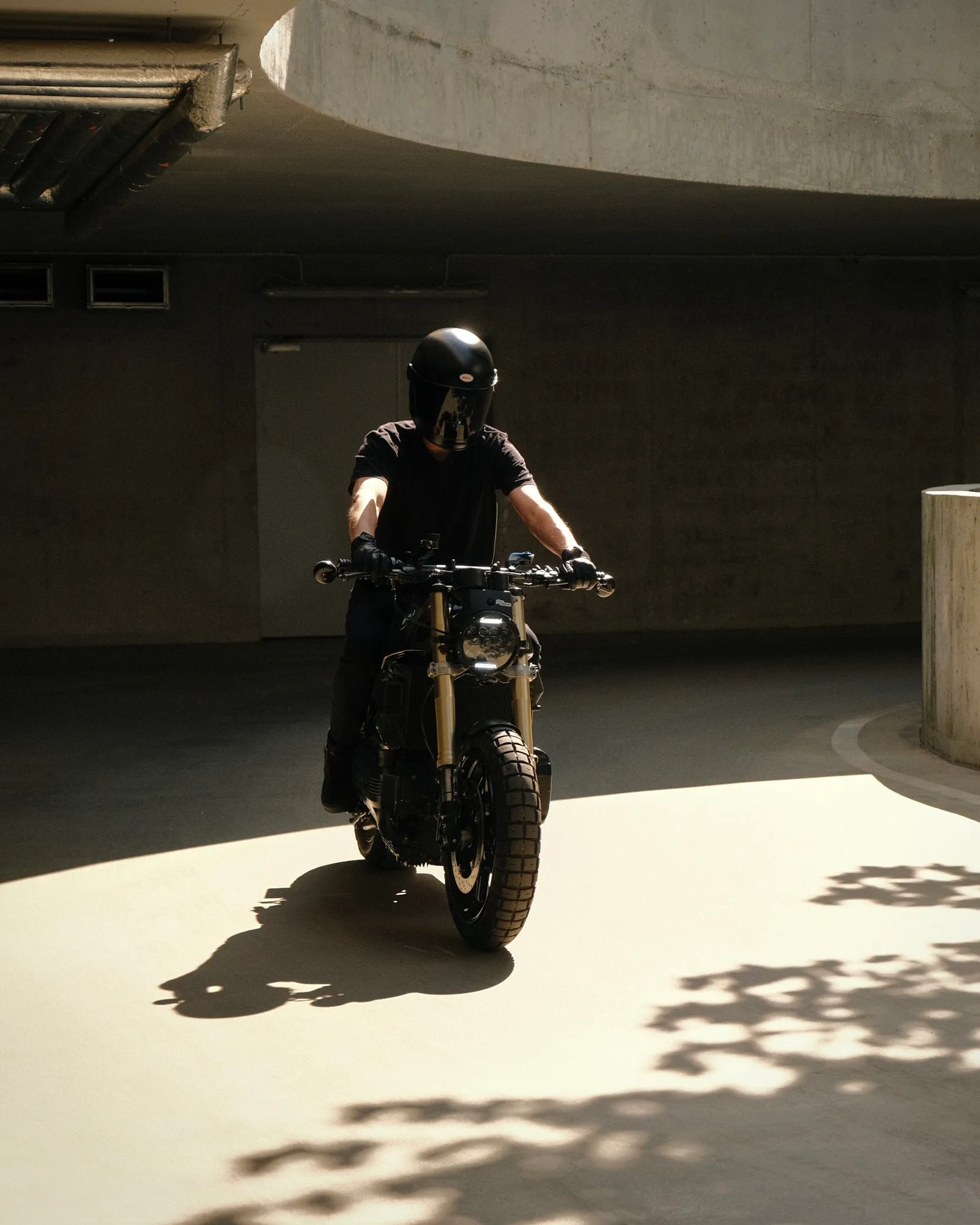 The K1100 ridden toward the camera through a concrete parking structure, LED headlight in shadow
