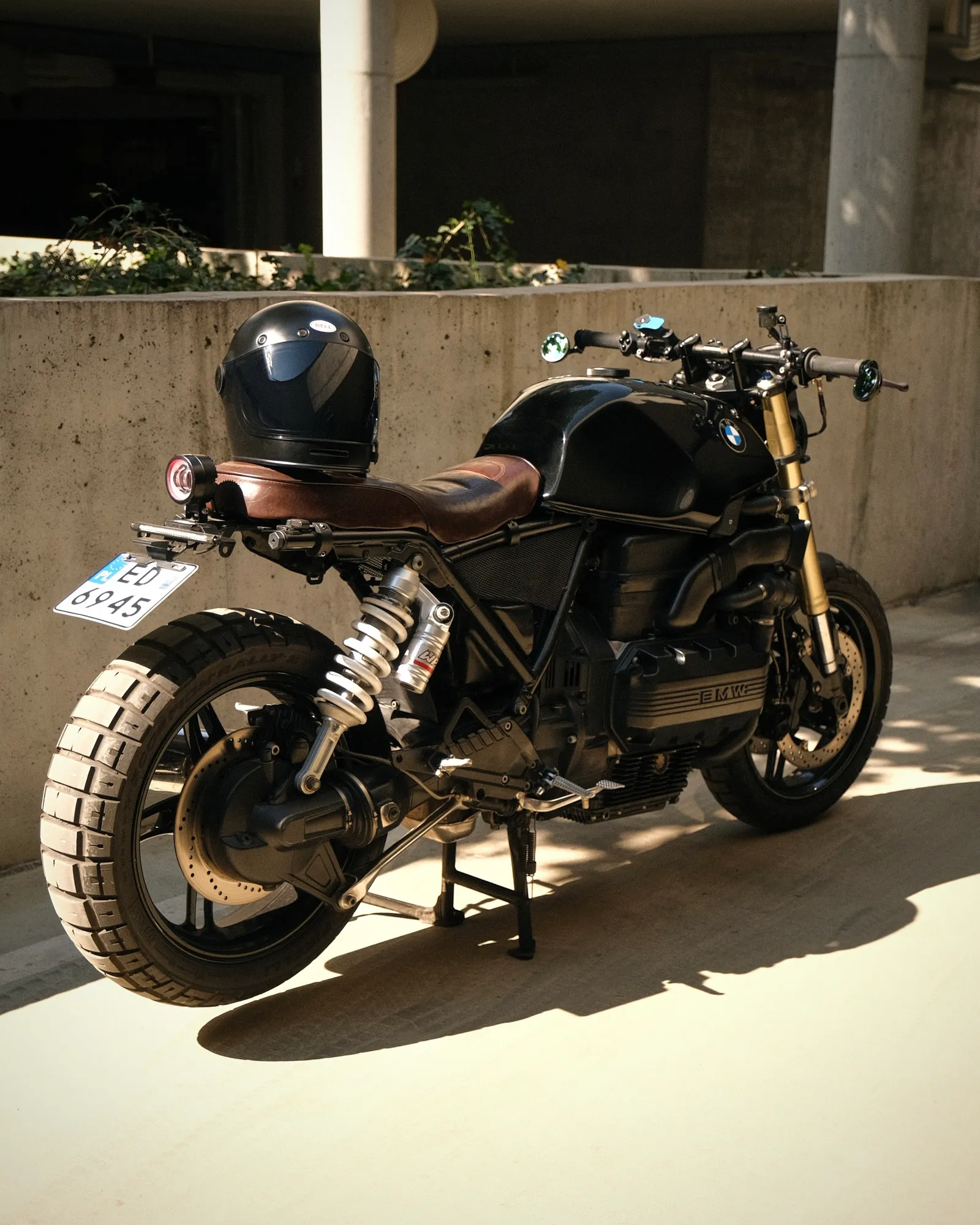 Rear three-quarter view of the black K1100 with brown leather seat, white-spring KTM shock and a helmet resting on the seat