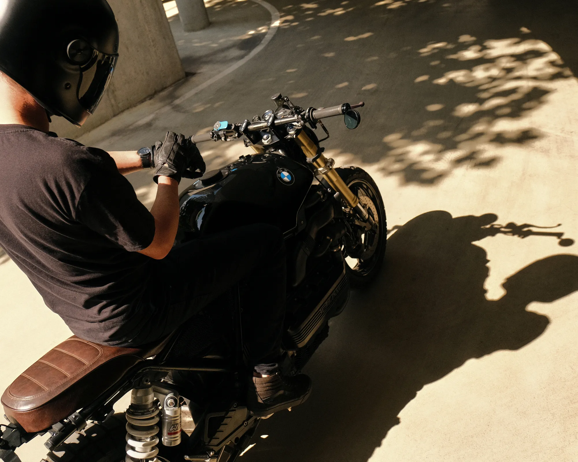 Top-down view over the handlebar of a black custom BMW K1100 with twin gauges, bar-end mirrors and a brown leather seat