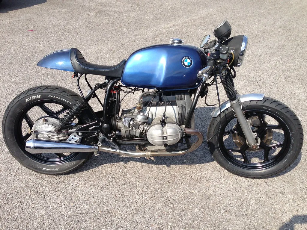 A blue BMW R80 cafe racer with a boxer engine and cafe seat parked on tarmac