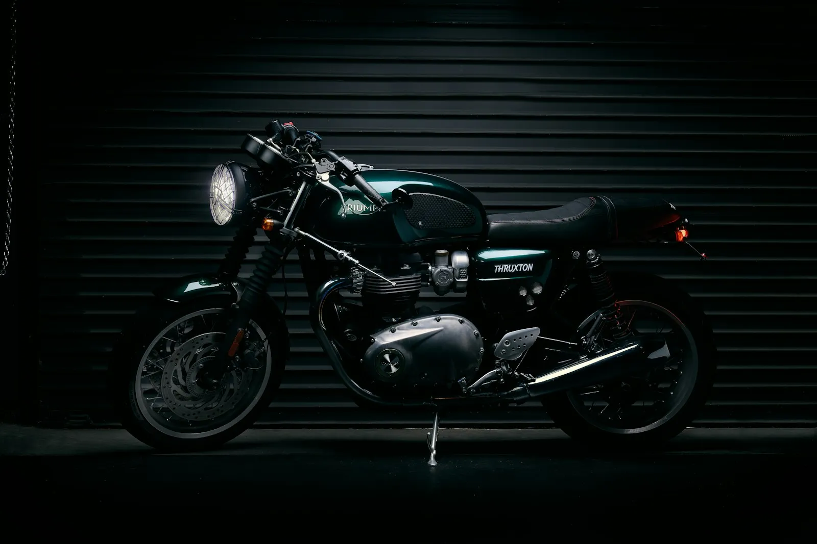 A dark green Triumph Thruxton cafe racer lit against a black roller door
