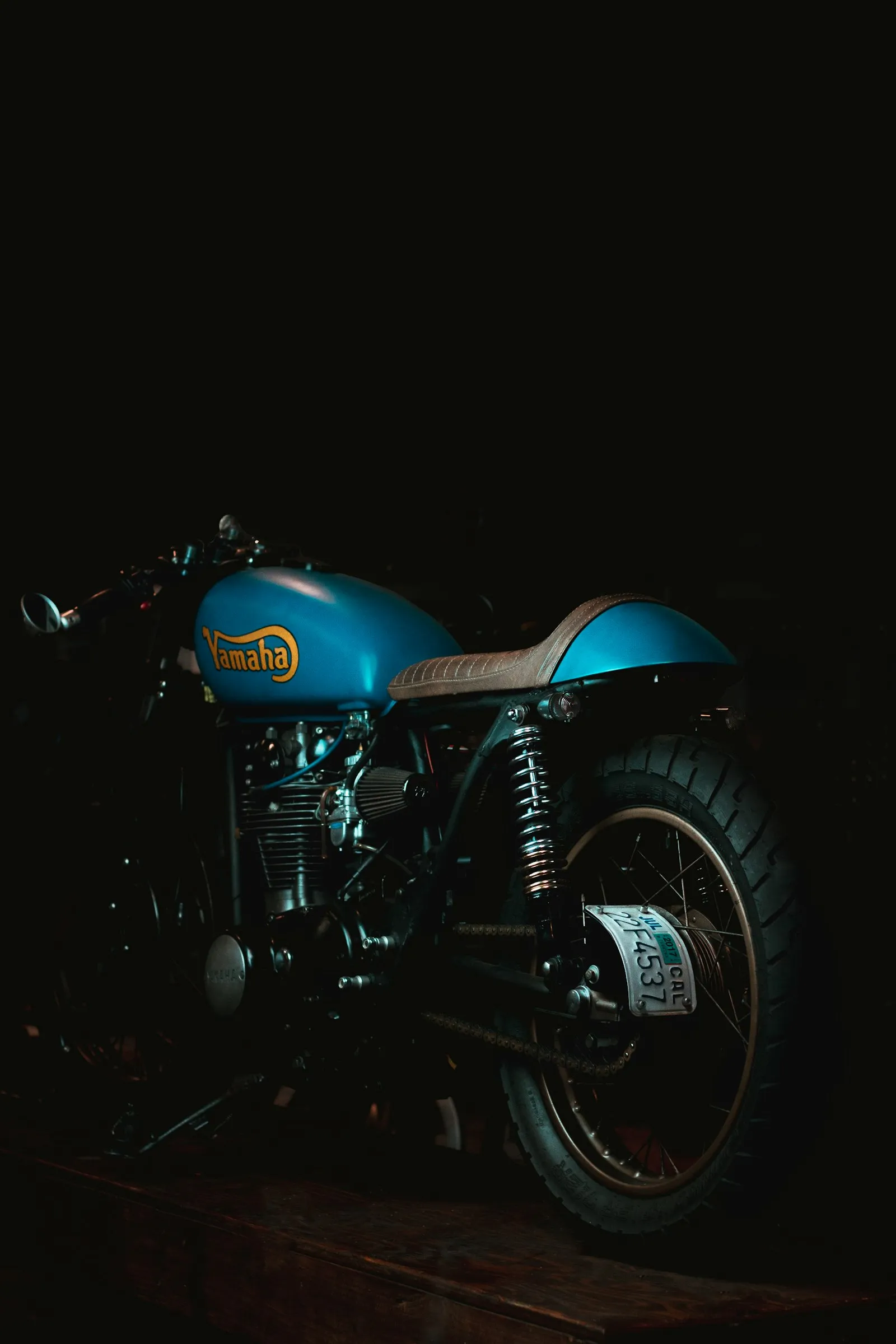 A blue Yamaha XS650 brat with a brown ribbed seat photographed in a dark workshop