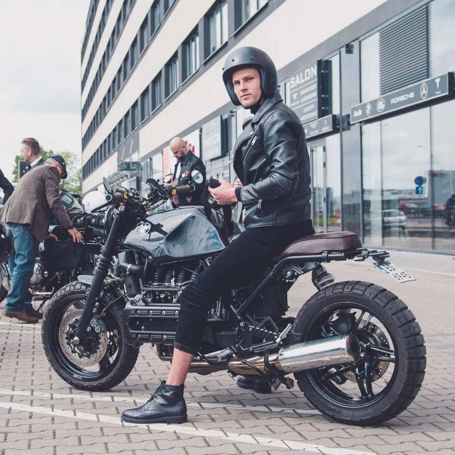 Rider in a leather jacket astride a BMW K-series brat on a Warsaw street