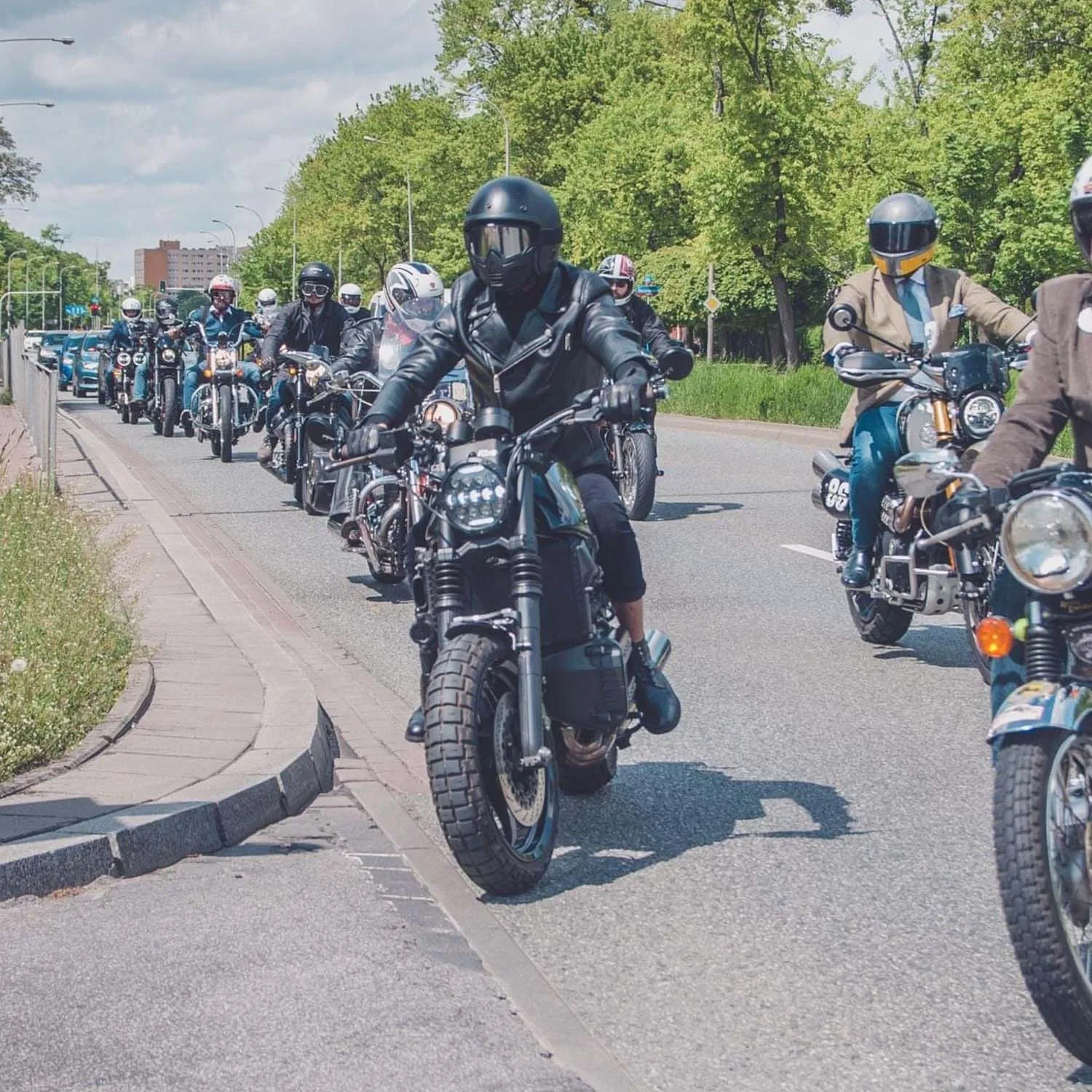 A pack of custom motorcycles riding two abreast down a tree-lined road