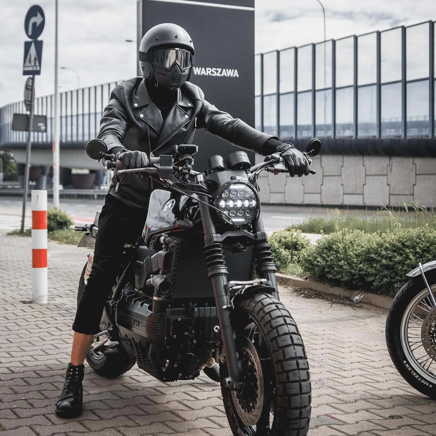 Helmeted rider on a BMW brat pulling away past a Warszawa road sign